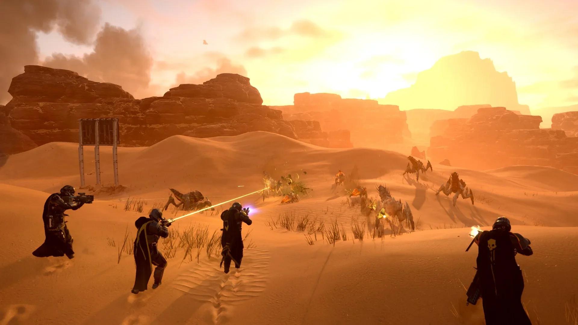 Four Helldivers in black capes fire at a swarm of Terminid bugs across orange desert dunes at sunset in Helldivers 2